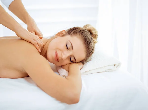 Young and blonde woman enjoying massage of back in spa salon. Beauty concept — Stock Photo, Image