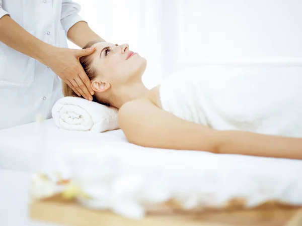 Young and blonde woman enjoying facial massage in spa salon. Beauty concept Royalty Free Stock Images