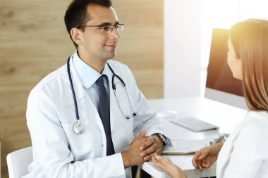 Doktor ve hasta güneşli klinikteki masada otururken tıbbi muayene sonuçlarını tartışıyorlar.