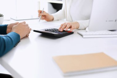 Mali durumu kontrol eden ya da vergi formları için hesap makinesinin geliri ile sayan, elleri yakın çekim. İş kadını ofisteki masada iş arkadaşıyla oturuyor ve çalışıyor. Vergi ve Denetim kavramı