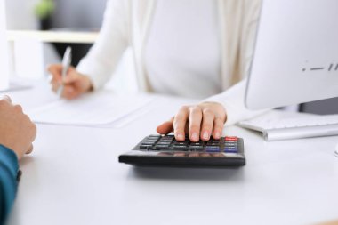 Mali durumu kontrol eden ya da vergi formları için hesap makinesinin geliri ile sayan, elleri yakın çekim. İş kadını ofisteki masada iş arkadaşıyla oturuyor ve çalışıyor. Vergi ve Denetim kavramı