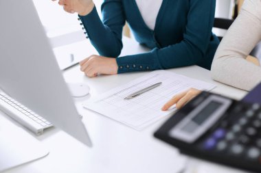 Mali durumu kontrol eden ya da vergi formları için hesap makinesinin geliri ile sayan, elleri yakın çekim. İş kadını ofisteki masada iş arkadaşıyla oturuyor ve çalışıyor. Vergi ve Denetim kavramı