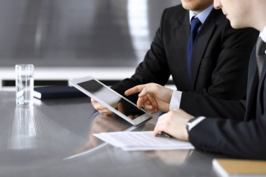 İşadamı tablet bilgisayar kullanıyor ve iş arkadaşı ya da ortağıyla modern ofiste cam masada çalışıyor. Yakın plan. Toplantıda bilinmeyen iş adamları var. Takım çalışması ve ortaklık kavramı