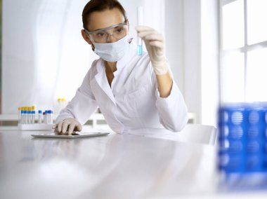 Kadın laboratuvar asistanı mavi sıvıyla test tüpünü analiz ediyor. Tıp, sağlık ve araştırma konsepti