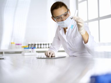Kadın laboratuvar asistanı mavi sıvıyla test tüpünü analiz ediyor. Tıp, sağlık ve araştırma konsepti