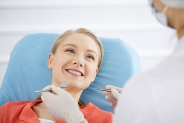 Gülümseyen beyaz kadın dişçi kliniğinde dişçi tarafından muayene ediliyor. Sağlıklı dişler ve ilaçlar, stomatoloji konsepti
