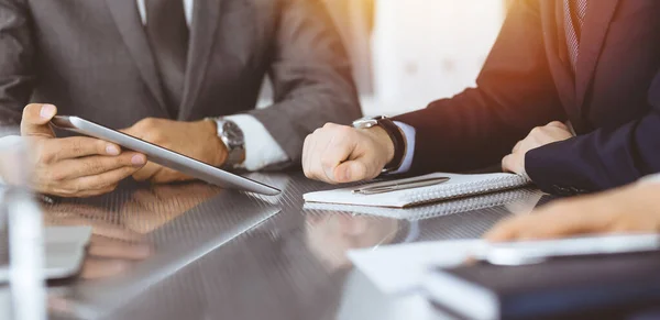 Unknown businessman using tablet computer and working together with his colleague while sits at the glass desk in modern office. Teamwork and partnership concept