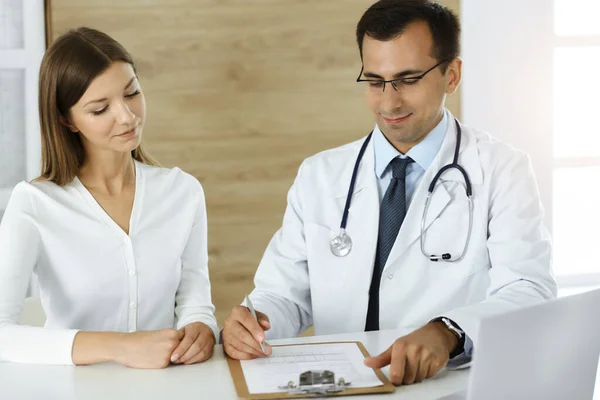 Doctor and patient discussing medical exam results while sitting at the desk in sunny clinic