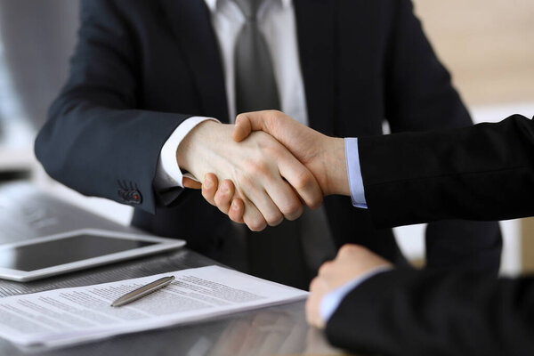 Businessman shaking hands with his colleague or partner above the glass desk in modern office, close-up. Unknown business people at meeting. Teamwork, partnership and handshake concept