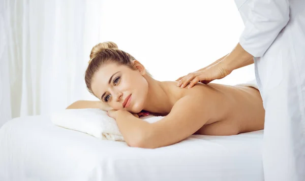 Young and blonde woman enjoying massage of back in spa salon. Beauty concept — Stock Photo, Image