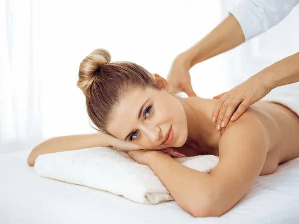 Young and blonde woman enjoying massage of back in spa salon. Beauty concept — Stock Photo, Image