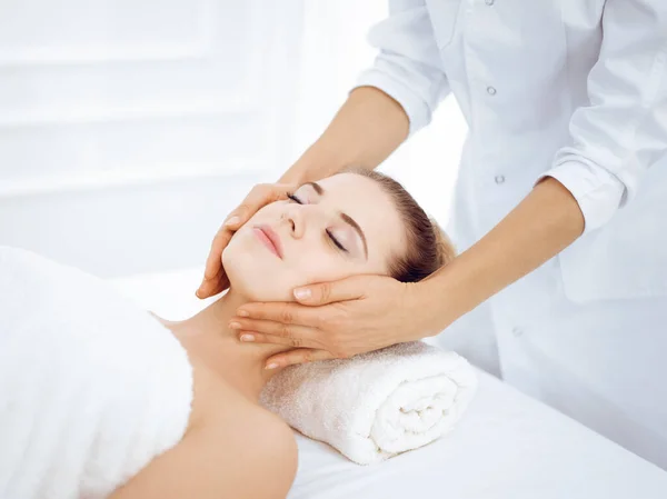 Young and blonde woman enjoying facial massage in spa salon. Beauty concept — Stock Photo, Image