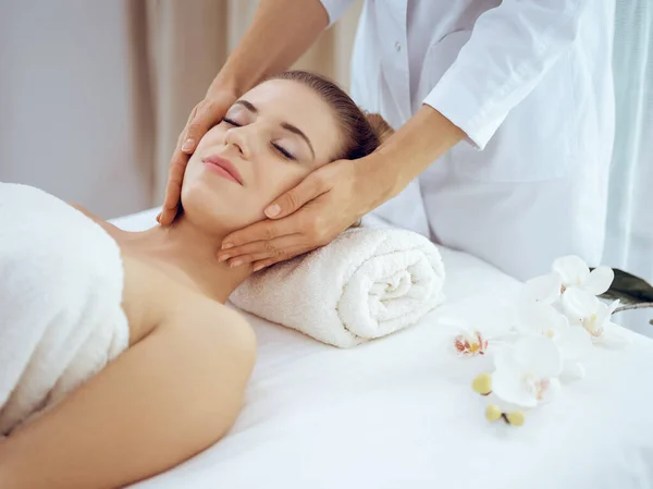 Jonge en blonde vrouw geniet van gezichtsmassage in spa salon. Schoonheidsconcept — Stockfoto