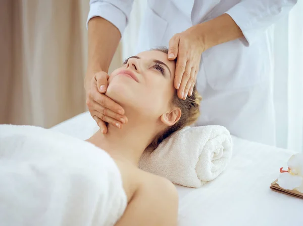 Young and blonde woman enjoying facial massage in spa salon. Beauty concept — Stock Photo, Image