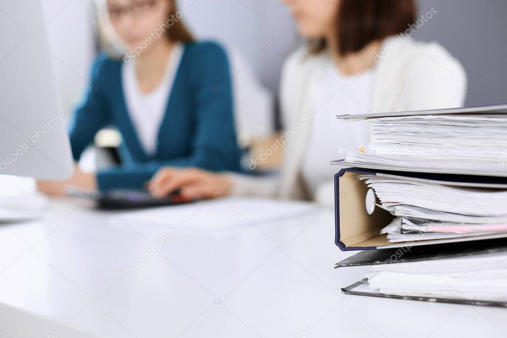 Binders with papers are waiting to be processed by business woman or bookkeeper working at the desk in office back in blur. Audit and tax concept