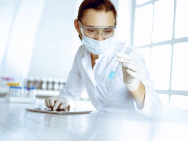 Kadın laboratuvar asistanı mavi sıvıyla test tüpünü analiz ediyor. Tıp, sağlık ve araştırma konsepti