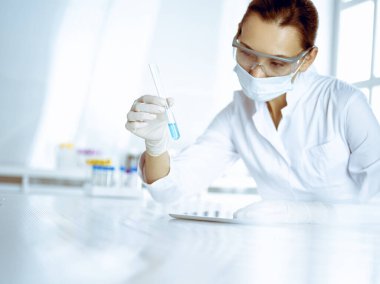 Kadın laboratuvar asistanı mavi sıvıyla test tüpünü analiz ediyor. Tıp, sağlık ve araştırma konsepti