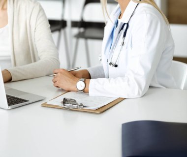 Bilinmeyen kadın doktor oturuyor ve kadın hastayla iletişim kuruyor. Doktor tıbbi geçmişi ve muayene sonuçlarını yakından kontrol ediyor. Sağlık hizmetleri kavramı