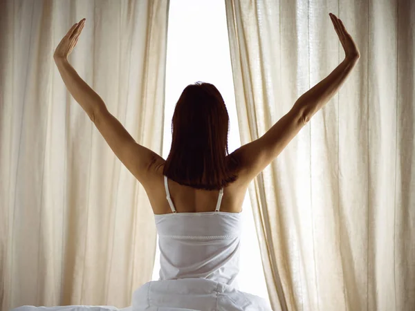 Kvinnan sträcker sig i sängen efter att ha vaknat, bakifrån, in i en dag glad och avslappnad efter god natts sömn. God morgon och ny dag för brunett. Begreppet helg, helgdagar — Stockfoto
