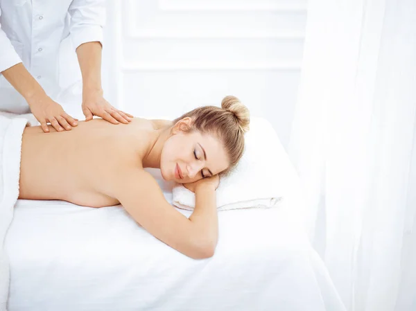 Ung och blond kvinna njuter av massage av tillbaka i spa salong. Skönhetsbegreppet — Stockfoto