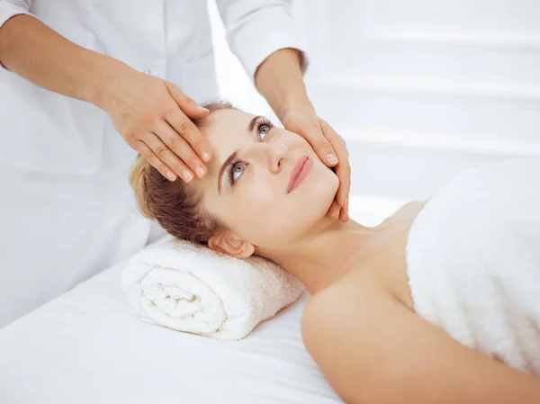 Jonge en blonde vrouw geniet van gezichtsmassage in spa salon. Schoonheidsconcept — Stockfoto