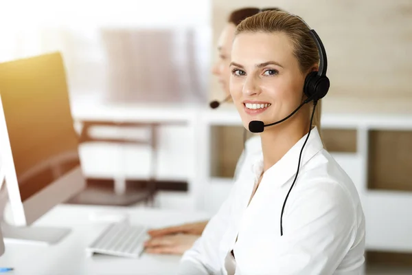 Blondynka przedstawiciel obsługi klienta konsultuje się z klientami online za pomocą zestawu słuchawkowego w słonecznym biurze. Koncepcja call center — Zdjęcie stockowe