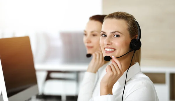 Loira representante de atendimento ao cliente do sexo feminino está consultando clientes on-line usando fone de ouvido no escritório ensolarado. Conceito de call center — Fotografia de Stock