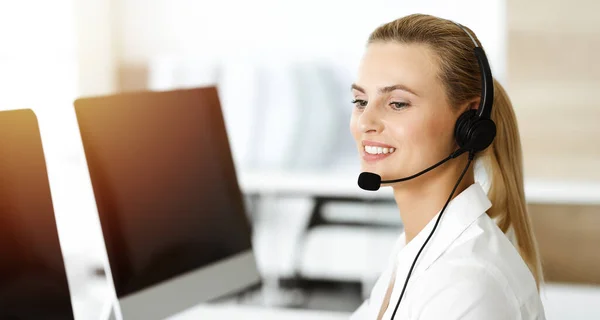 Blond kvinnlig kundtjänst representant konsulterar kunder online med headset i soligt kontor. Begreppet callcenter — Stockfoto