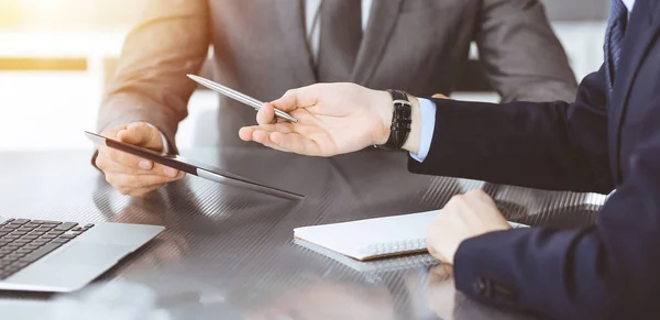 Hombre de negocios desconocido que utiliza la computadora de la tableta y el trabajo junto con su colega mientras se sienta en el escritorio de cristal en la oficina moderna. Trabajo en equipo y concepto de asociación — Foto de Stock