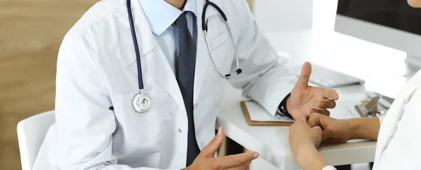 Onbekende arts en patiënt bespreken iets terwijl ze aan het bureau zitten in de kliniek, close-up. Concept van de geneeskunde en comfortabele service in de kliniek — Stockfoto