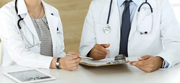 Twee onbekende artsen bespreken behandelingsproblemen terwijl ze aan het bureau zitten in het ziekenhuiskantoor, close-up. Gegevens in de geneeskunde — Stockfoto