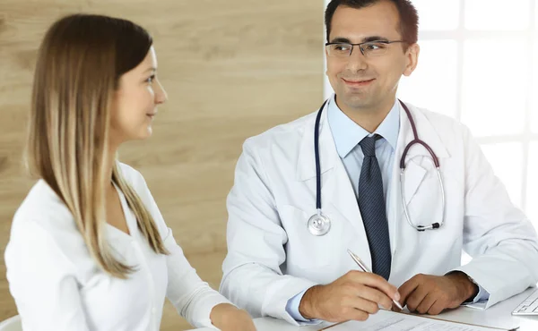 Médico y paciente discutiendo los resultados del examen médico mientras está sentado en el escritorio en la clínica soleada — Foto de Stock