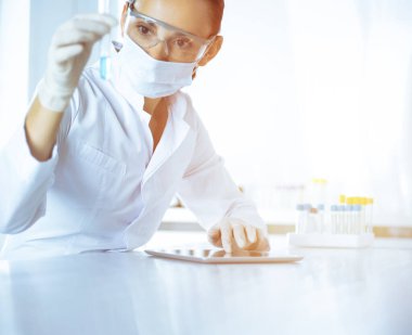 Kadın laboratuvar asistanı mavi sıvıyla test tüpünü analiz ediyor. Tıp, sağlık ve araştırma konsepti