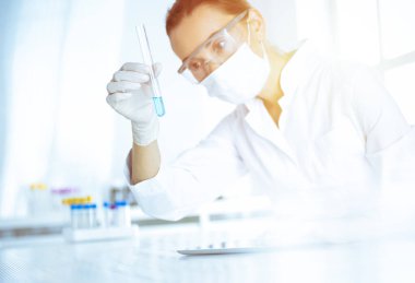 Kadın laboratuvar asistanı mavi sıvıyla test tüpünü analiz ediyor. Tıp, sağlık ve araştırma konsepti