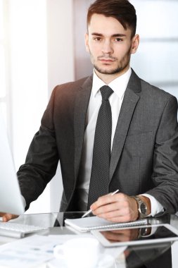 Güneşli ofiste bilgisayarla çalışan bir iş adamı. İş yerindeki erkek girişimcinin vesikalığı. İş konsepti