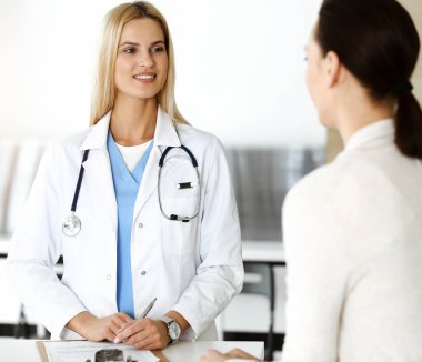 Sunny Hastanesi 'ndeki kadın doktor kadın hastaya danışmaktan mutluluk duyar. Sarışın doktor, pano kullanırken tıbbi geçmişi ve sınav sonuçlarını kontrol ediyor.