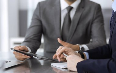 Bilinmeyen işadamı, modern ofisteki cam masada otururken tablet bilgisayar kullanıyor ve iş arkadaşıyla birlikte çalışıyor. Takım çalışması ve ortaklık kavramı