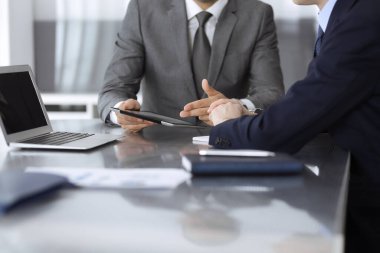 Bilinmeyen işadamı, modern ofisteki cam masada otururken tablet bilgisayar kullanıyor ve iş arkadaşıyla birlikte çalışıyor. Takım çalışması ve ortaklık kavramı