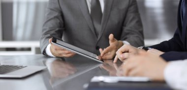 Bilinmeyen işadamı, modern ofisteki cam masada otururken tablet bilgisayar kullanıyor ve iş arkadaşıyla birlikte çalışıyor. Takım çalışması ve ortaklık kavramı