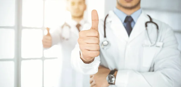 Two male doctors standing as a team with thumbs up in hospital office and ready to help patients. Medical help, best disease treatment and medicine concept