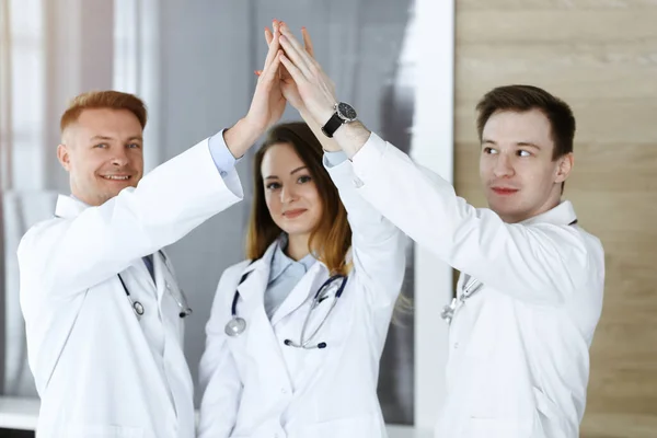 Grupa nowoczesnych lekarzy stojąca w zespole, łącząca ręce lub dająca sobie nawzajem pięć. Lekarze gotowi do badania i pomocy pacjentom. Pomoc medyczna, ubezpieczenie w opiece zdrowotnej, najlepsze leczenie i — Zdjęcie stockowe