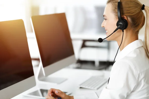 Blond female customer service representative is consulting clients online using headset in sunny office. Call center concept — Stock Photo, Image