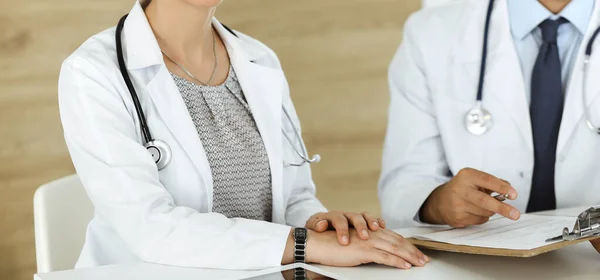 Due medici sconosciuti discutono di problemi di trattamento mentre sono seduti alla scrivania nell'ufficio dell'ospedale, primo piano. Dati in medicina — Foto Stock