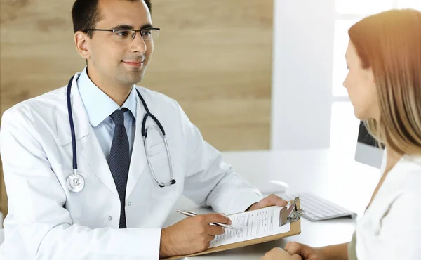 Médico y paciente discutiendo los resultados del examen médico mientras está sentado en el escritorio en la clínica soleada — Foto de Stock