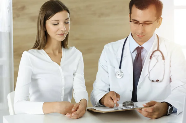 Médico y paciente discutiendo los resultados del examen médico mientras está sentado en el escritorio en la clínica soleada — Foto de Stock