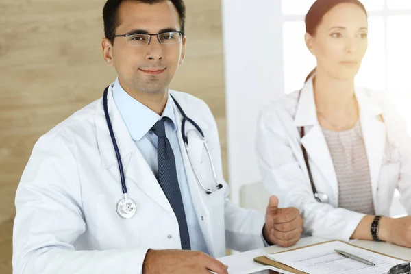 Två läkare diskuterar behandlingsproblem medan du sitter vid skrivbordet på soligt kontor — Stockfoto
