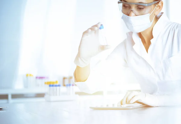 Female laboratory assistant analyzing a blood sample at hospital. Medicine, health care and researching concept — Stock Photo, Image