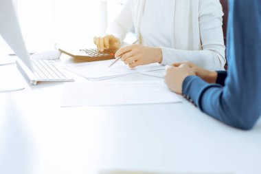 Muhasebeci mali durumu kontrol ediyor ya da vergi formları için hesap makinesi geliri ile sayıyor, eller yakın çekim. İş kadını ofisteki masada iş arkadaşıyla oturuyor ve çalışıyor. Denetim kavramı