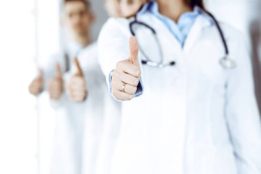 Bir grup modern doktor hastane ofisinde baş parmakları havada bir takım gibi duruyorlar. Tıbbi yardım, sağlık sigortası, en iyi hastalık tedavisi ve ilaç konsepti