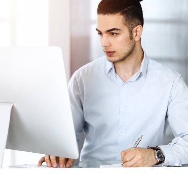 İşadamı güneşli ofiste bilgisayarla çalışıyor. Arap erkek girişimcinin iş yerindeki vesikalığı